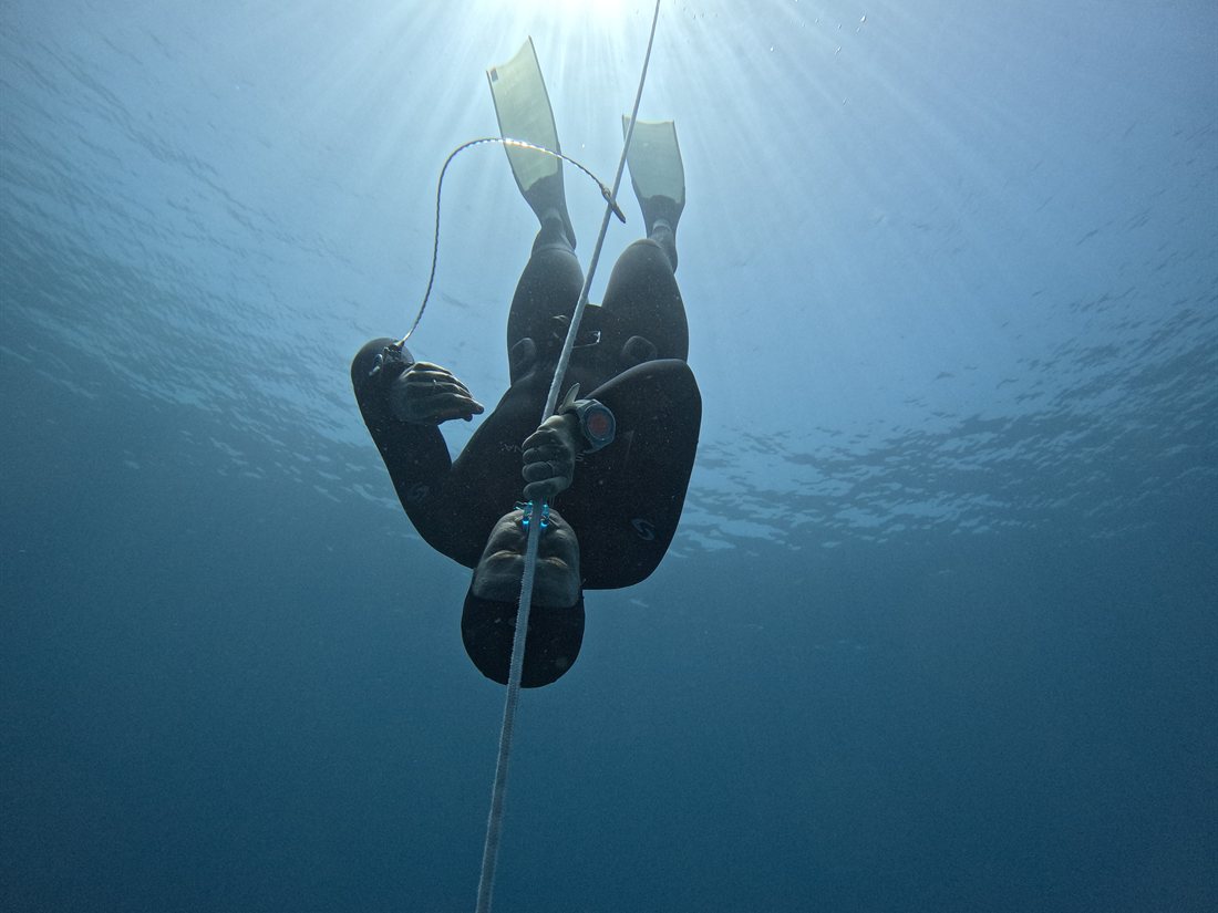 A calm freediver underwater, face relaxed, sunlight filtering down from the surface