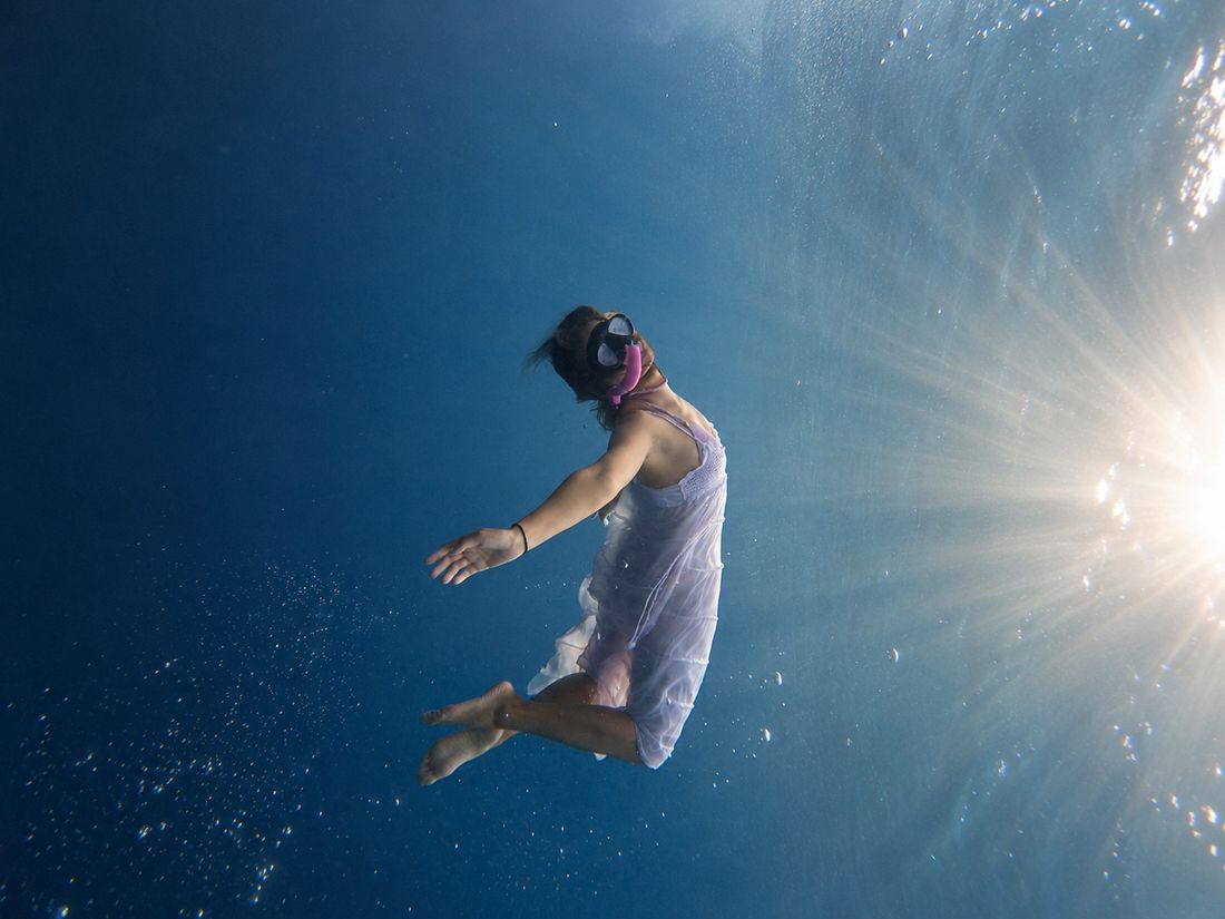 A freediver descending through the sun rays