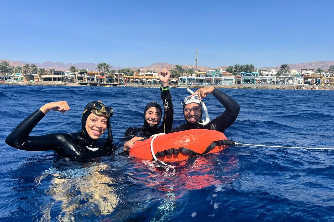 Three freedivers celebrating at the buoy off the Lighthouse, with the Dahab shoreline behind