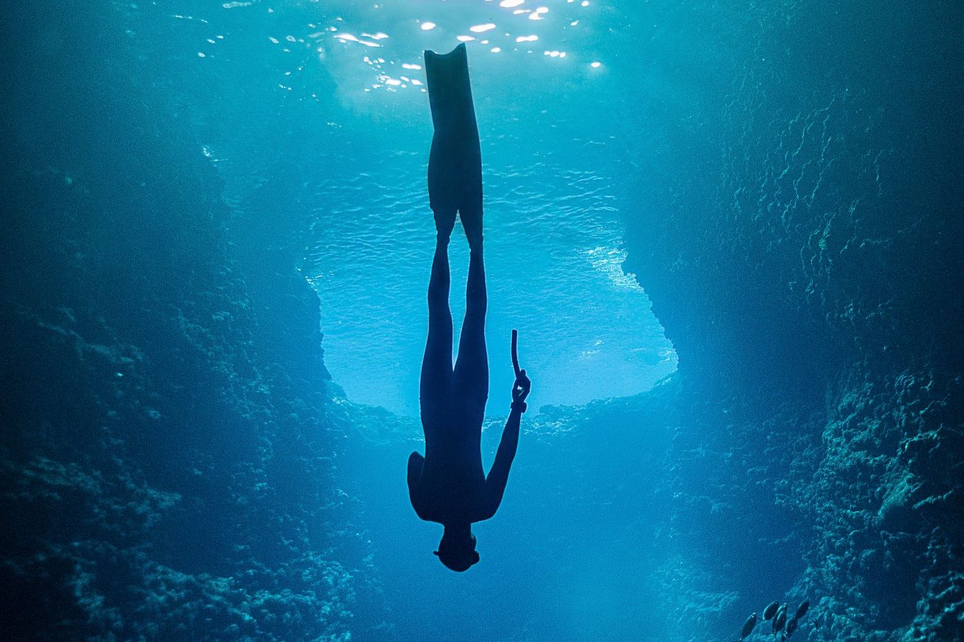 A freediver descending through volcanic rock formations in clear Atlantic water